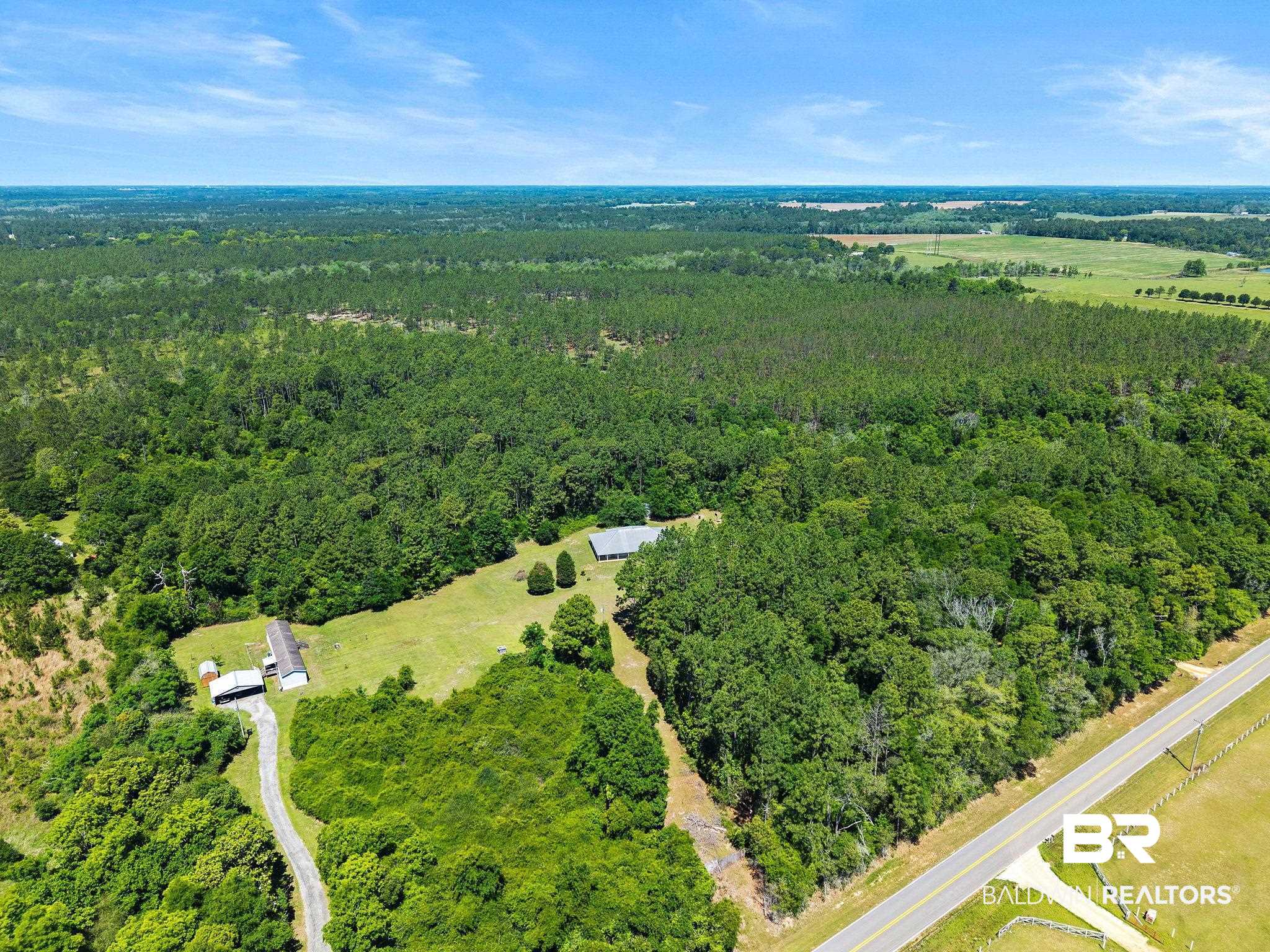 20219 Greek Cemetery Road Robertsdale, AL 36567 - Photo 39 of 41 Expansive rural property featuring a vast tree-covered landscape, open fields, a paved road frontage, and two visible structures