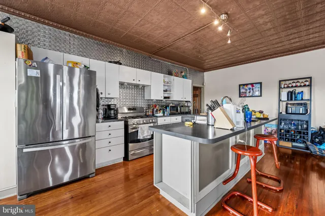 a kitchen with stainless steel appliances granite countertop a refrigerator a stove a sink dishwasher and white cabinets with wooden floor