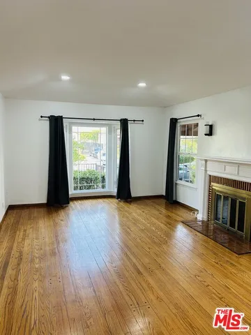 an empty room with wooden floor fireplace and windows