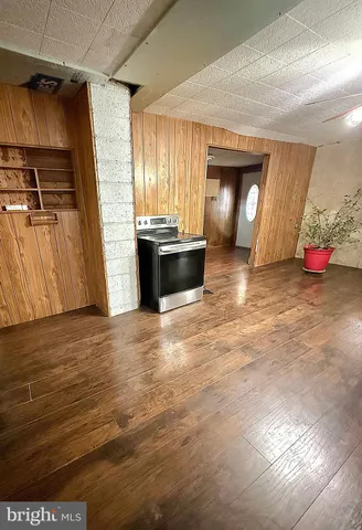 a view of an empty room with wooden floor and kitchen view
