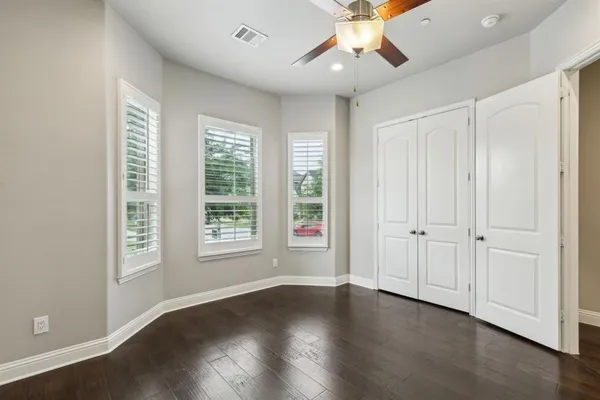 an empty room with wooden floor fan and windows