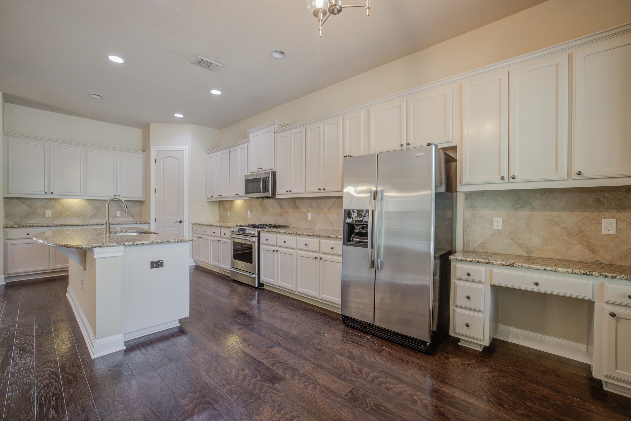 4524 Berkman Drive Austin, TX 78723 - Photo 11 of 38 Kitchen featuring an island with a double basin sink, white cabinetry, stainless steel appliances, granite countertops, and wood-finish flooring