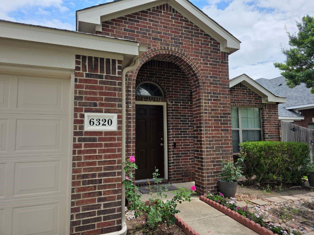 6320 Spring Ranch Drive Fort Worth, TX 76179 - Photo 2 of 24 Brick exterior featuring an arched entryway, a paneled garage door, a covered porch, a concrete walkway, and established landscaping