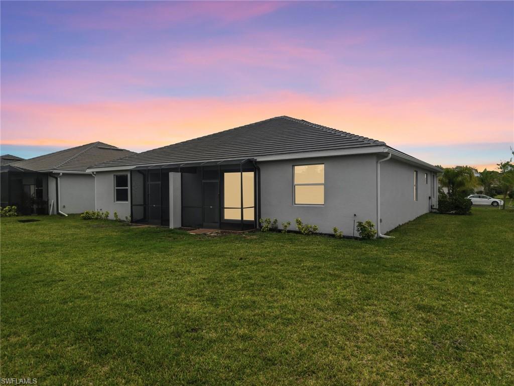 2224 Dragonfruit Way Naples, FL 34120 - Photo 26 of 33 Back of house at dusk featuring a lawn, a sunroom, and stucco siding
