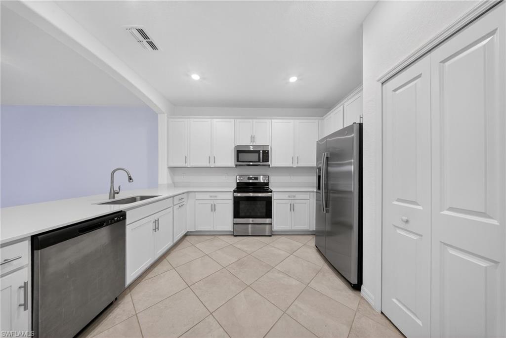 2224 Dragonfruit Way Naples, FL 34120 - Photo 3 of 33 Kitchen featuring stainless steel appliances, white cabinets, light tile patterned flooring, recessed lighting, and light stone counters