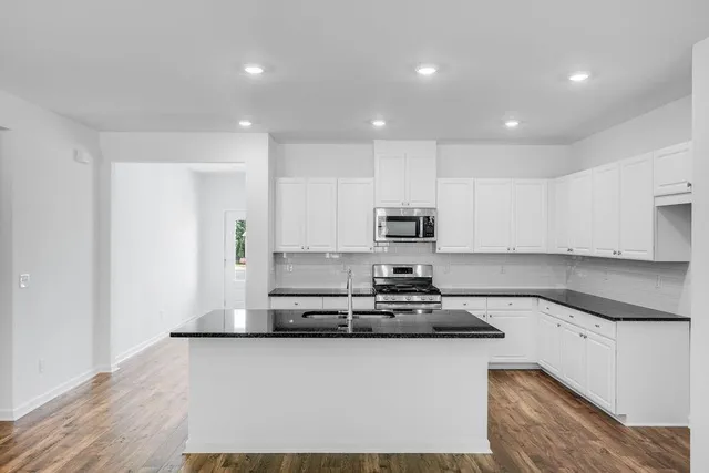 a kitchen with stainless steel appliances granite countertop a sink a stove a refrigerator a microwave and white cabinets