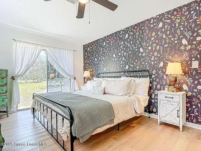 a bedroom with a bed next to a large window with wooden floor