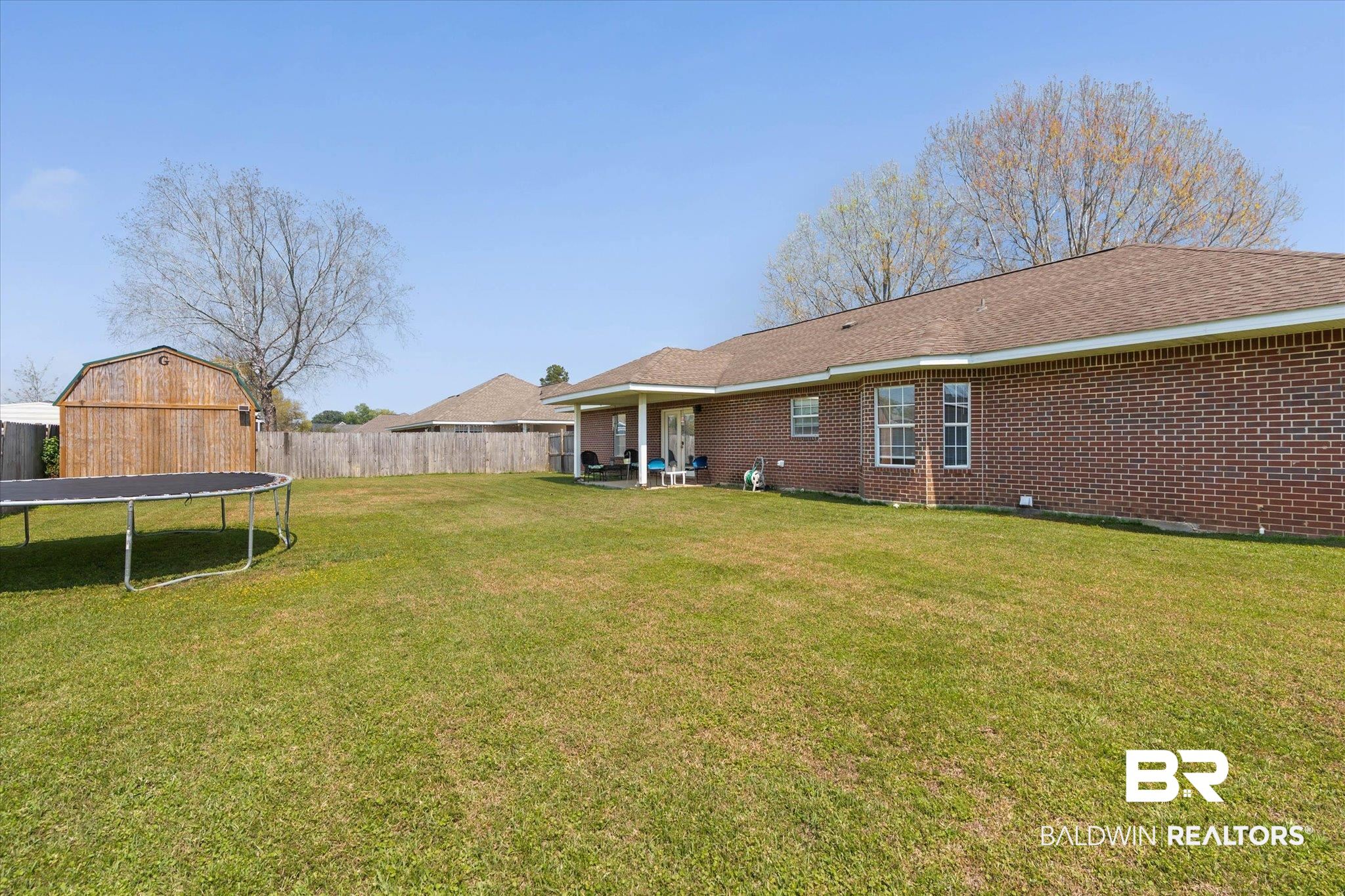 22095 Buck Road Robertsdale, AL 36567 - Photo 21 of 22 Rear view of house featuring a patio area, a trampoline, brick siding, and roof with shingles