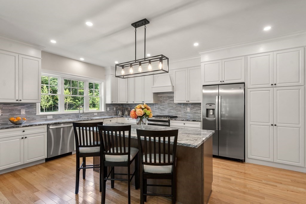 3 Emmeline Path, Unit 3 Wayland, MA 01778 - Photo 4 of 22 a kitchen with stainless steel appliances granite countertop a table chairs refrigerator and wooden cabinets