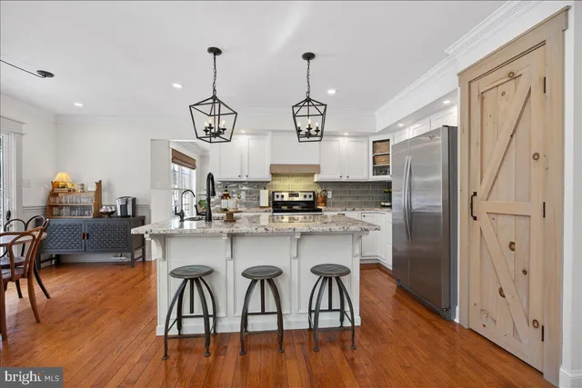 a kitchen with stainless steel appliances granite countertop a dining table chairs refrigerator and wooden floor
