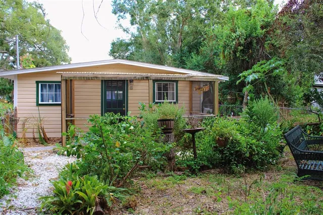 a view of a yard in front of a house with plants and large trees
