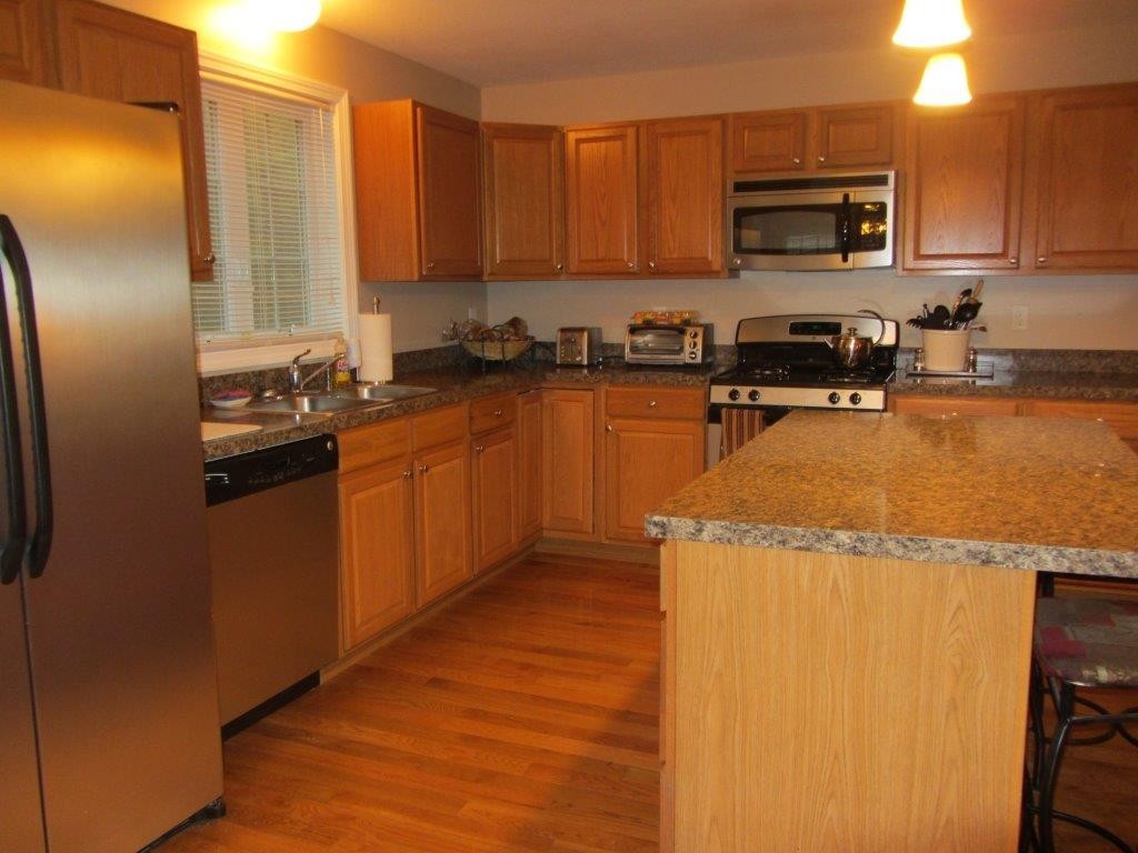 1161 B Mammoth Road, Unit B Pelham, NH 03076 - Photo 3 of 14 a kitchen with stainless steel appliances granite countertop a refrigerator a stove top oven a sink and dishwasher