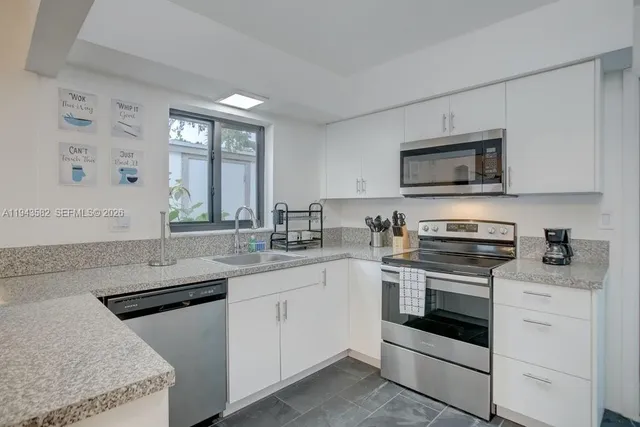 a kitchen with granite countertop white cabinets sink and stainless steel appliances