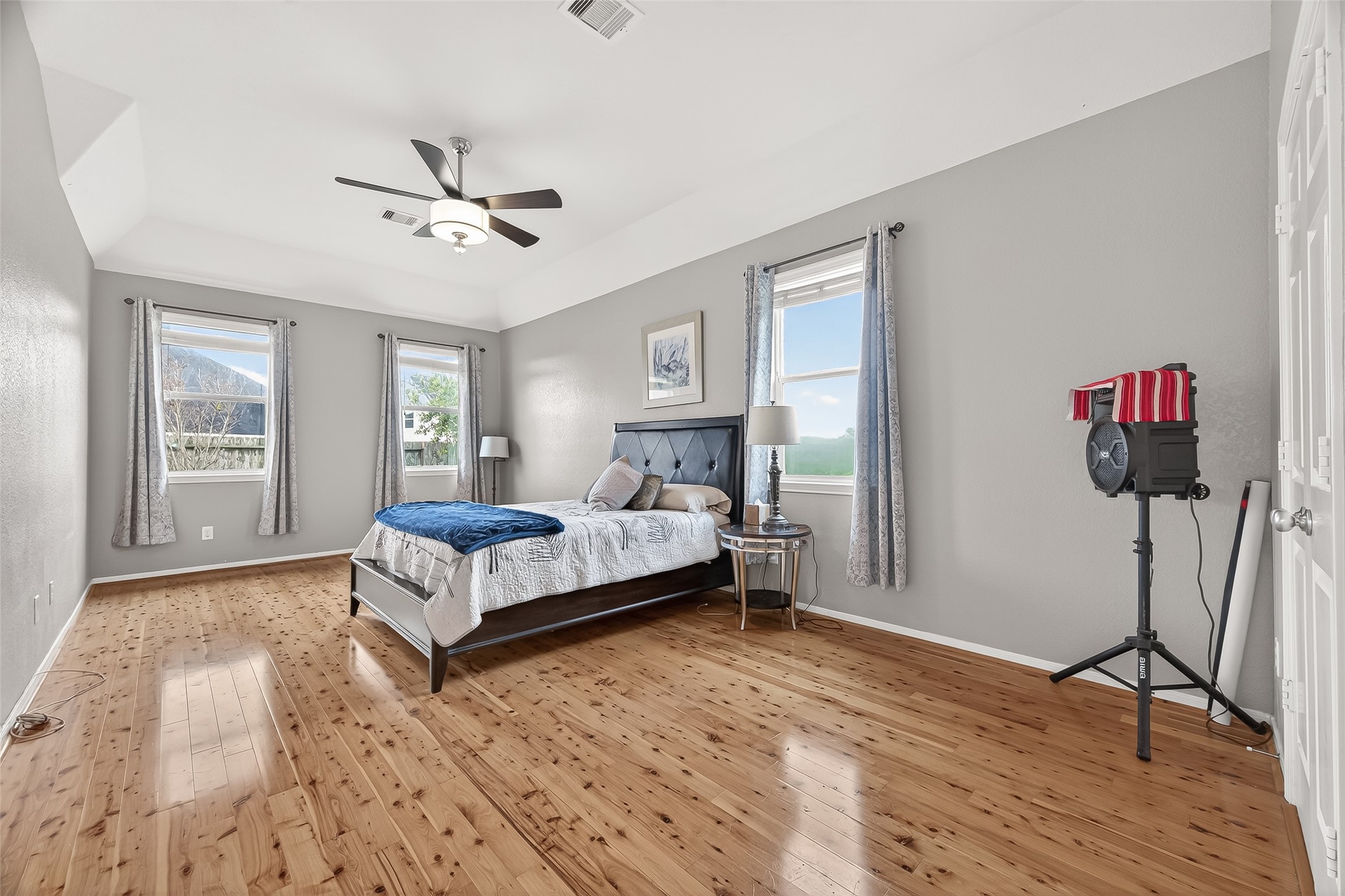 9110 Cavalier Lane Rosenberg, TX 77469 - Photo 22 of 30 Spacious and bright primary bedroom with wood flooring, neutral walls, and a modern ceiling fan. Features three large windows for natural lighting.