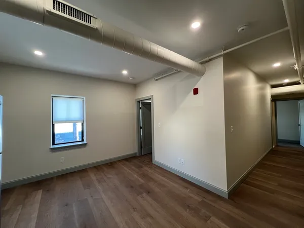 a view of an empty room with wooden floor and a window