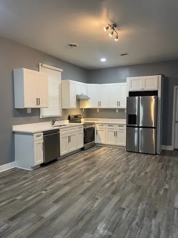 a large kitchen with stainless steel appliances granite countertop a stove a sink dishwasher a refrigerator and white cabinets with wooden floor
