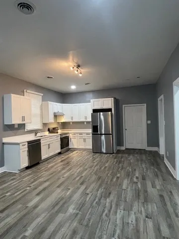a large white kitchen with a stove a sink dishwasher and a refrigerator with wooden floor