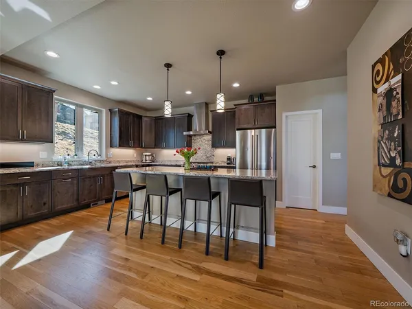 a kitchen with stainless steel appliances kitchen island granite countertop a refrigerator a stove a sink a dining table and chairs with wooden floor