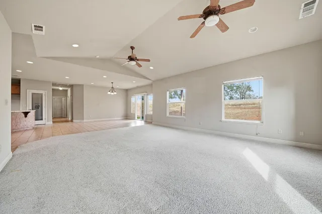 an empty room with a kitchen space and ceiling fan