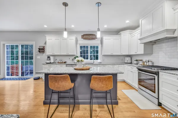 a kitchen with granite countertop a stove a sink a dining table and chairs with wooden floor
