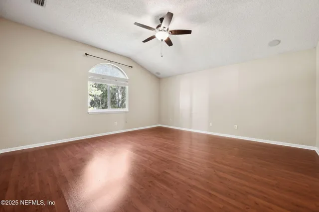a view of an empty room with wooden floor and a ceiling fan