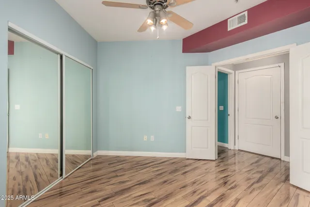 a view of an empty room with wooden floor and a ceiling fan