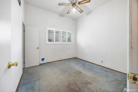 an empty room with chandelier fan and windows