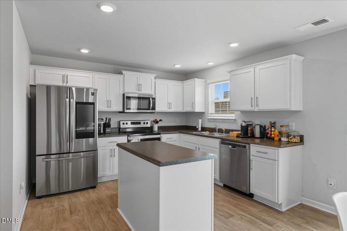 6854 Summerside Drive Whitsett, NC 27377 - Photo 18 of 49 a kitchen with granite countertop a refrigerator a sink dishwasher and a stove top oven with wooden floor