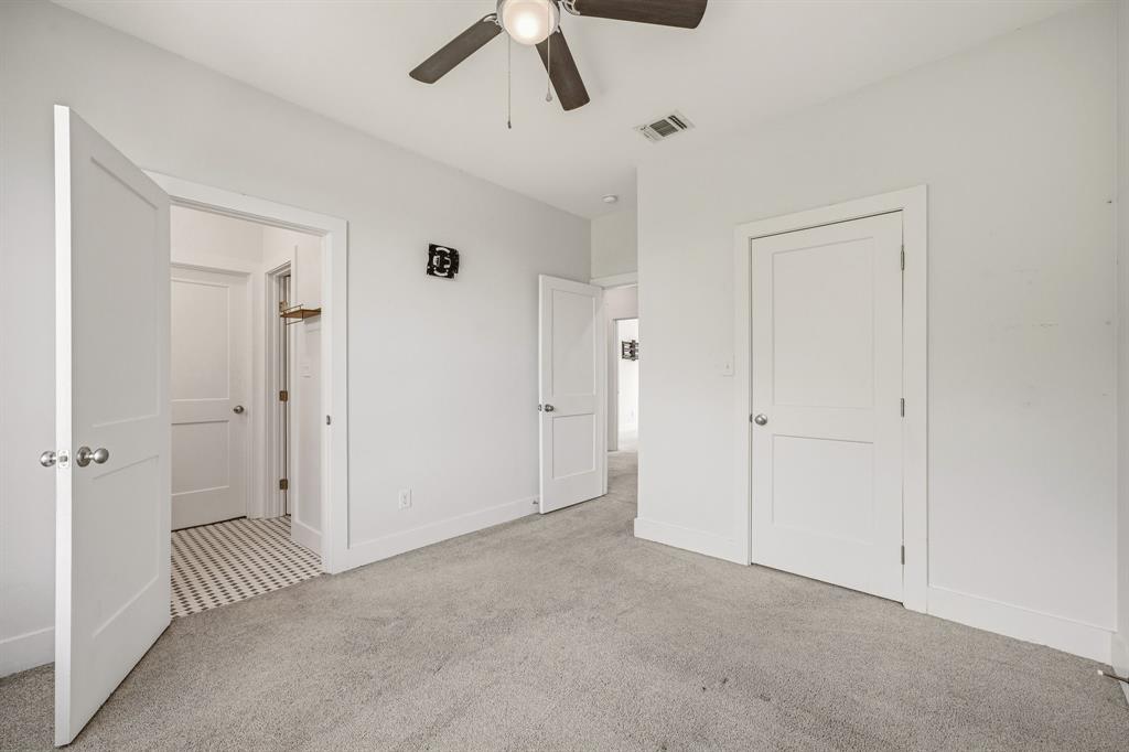 745 North Miller Avenue Stephenville, TX 76401 - Photo 20 of 31 Light gray carpeting with white baseboards, a ceiling fan with dark wood-finish blades, white two-panel interior doors with brushed nickel hardware, and a closet with a patterned tile floor