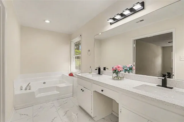 a bathroom with a tub sink double vanity and a mirror