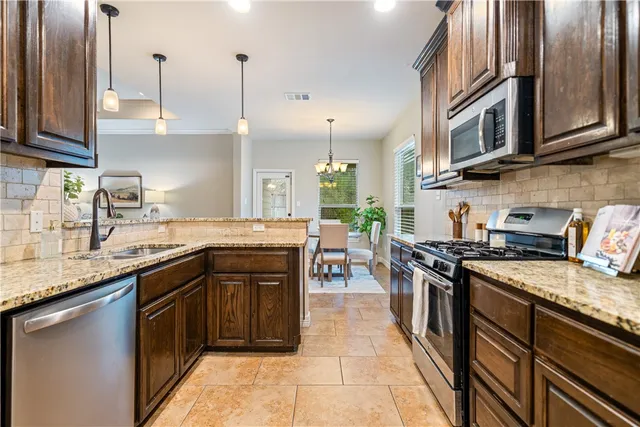 a kitchen with stainless steel appliances granite countertop a sink a stove and a wooden cabinets