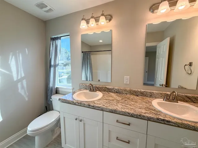 a bathroom with a granite countertop double vanity sink toilet and a mirror