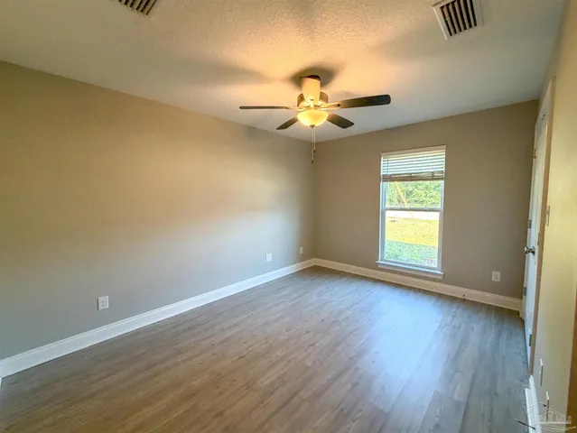 an empty room with wooden floor fan and windows