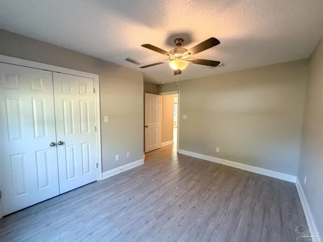 an empty room with wooden floor fan and windows