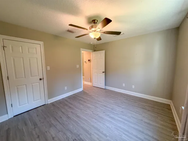 an empty room with wooden floor fan and windows