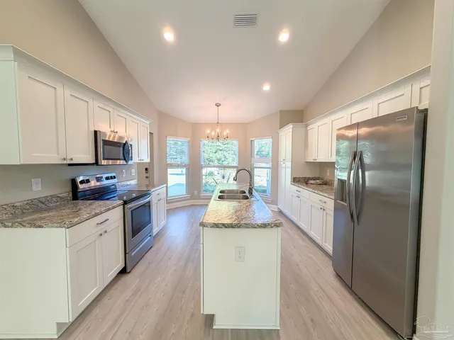 a kitchen with stainless steel appliances granite countertop a refrigerator a stove top oven a sink dishwasher and white cabinets with wooden floor