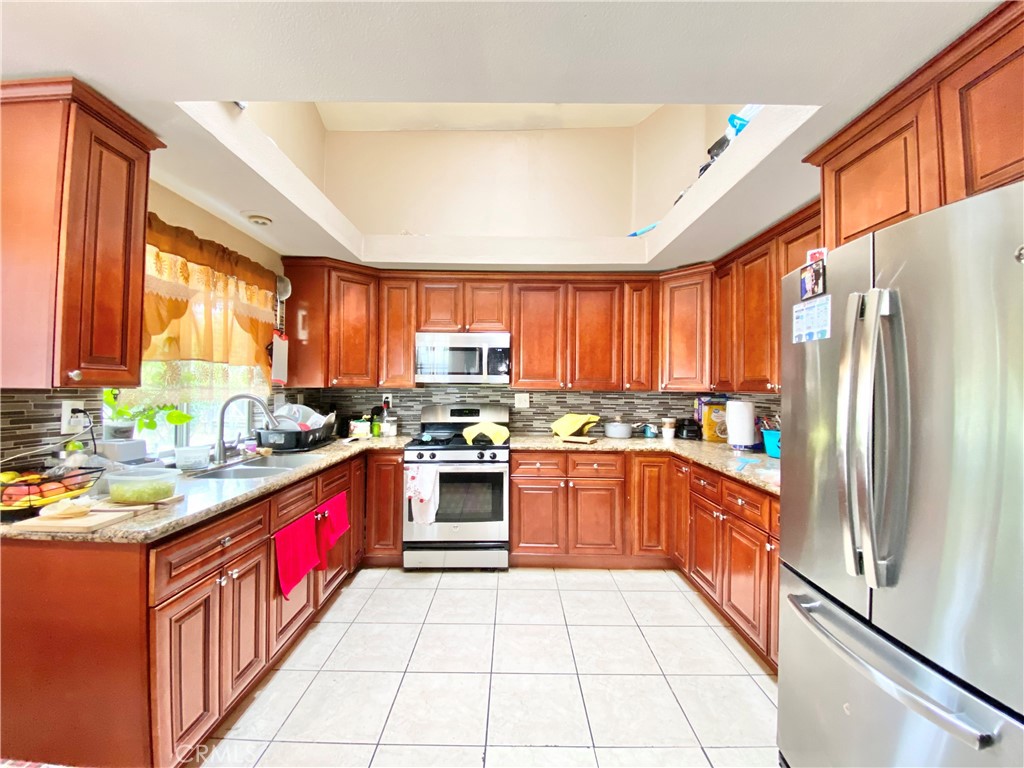 1444 North Sage Avenue Rialto, CA 92376 - Photo 8 of 22 a kitchen with stainless steel appliances granite countertop a refrigerator a sink dishwasher a stove with wooden cabinets and a dining table