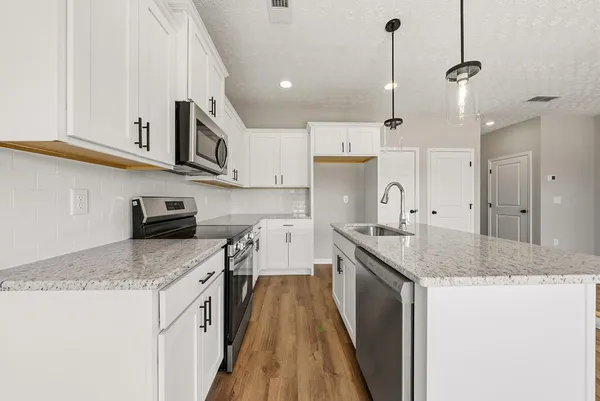 a kitchen with a sink dishwasher a stove a refrigerator and white cabinets with wooden floor