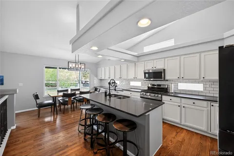 a kitchen with stainless steel appliances granite countertop a stove top oven a sink dishwasher a dining table and chairs with wooden floor