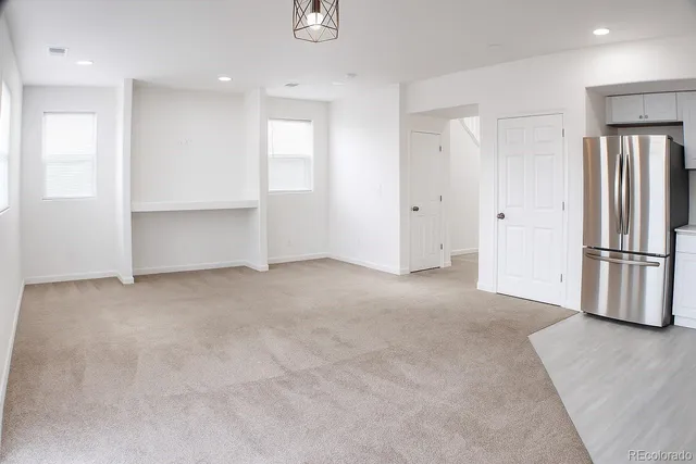 a view of an empty room with wooden floor and a kitchen