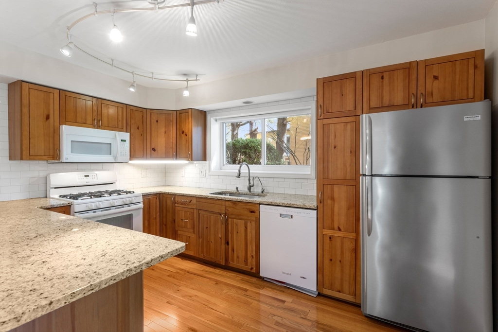 106 Captain Eames Circle, Unit 106 Ashland, MA 01721 - Photo 5 of 21 a kitchen with stainless steel appliances granite countertop a refrigerator a sink dishwasher a stove with wooden cabinets and floors