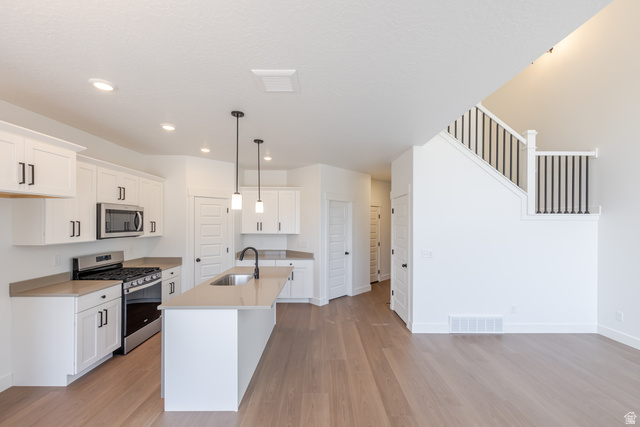 5224 South Acacia Drive, Unit 809 Mapleton, UT 84664 - Photo 13 of 23 Open-concept kitchen featuring an island with a sink and pendant lighting, white cabinetry with black hardware, stainless steel appliances, and light-toned countertops