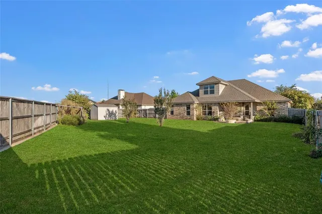 a view of a white house in front of a big yard with plants and large trees