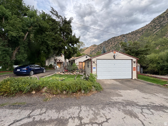 Detached garage with a paneled door, mature trees, and a mountain backdrop