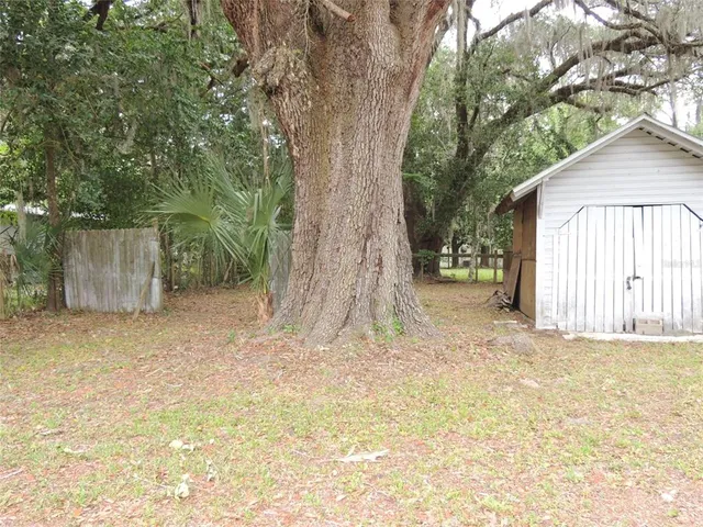 a backyard of a house with large trees and wooden fence