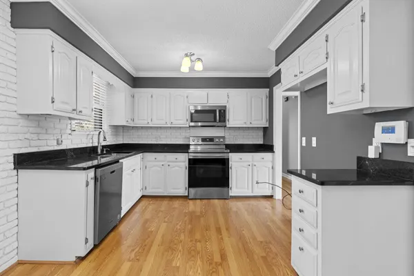 a kitchen with granite countertop a stove top oven a sink dishwasher and a microwave oven with white cabinets