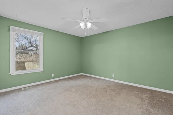an empty room with chandelier fan and windows