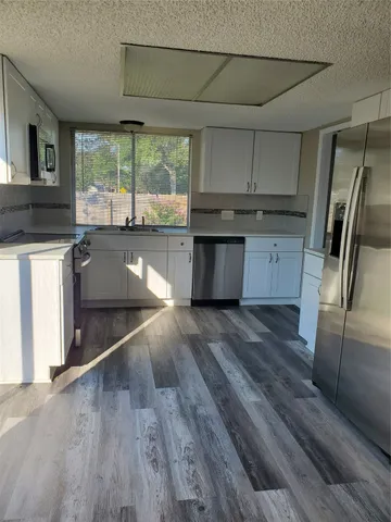 a kitchen with stainless steel appliances granite countertop a refrigerator a sink dishwasher a stove and white countertops with wooden floor