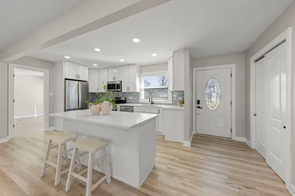 a kitchen with granite countertop a refrigerator oven a sink dishwasher and white cabinets with wooden floor