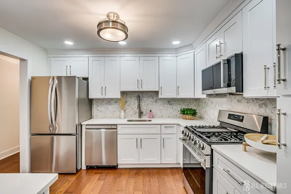 a kitchen with stainless steel appliances a sink dishwasher a refrigerator and white cabinets with wooden floor